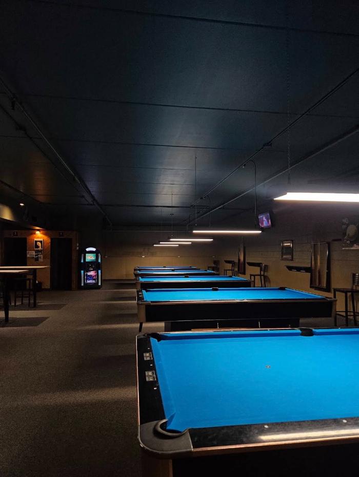 Row of blue-felt billiards tables under hanging lights at End Pocket